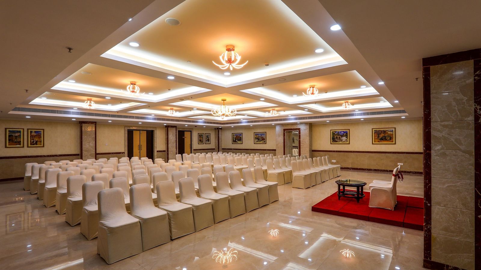 Front view of white chairs and a well-lit ceiling at Banquet Hall in Hotel Aadithya, Chennai