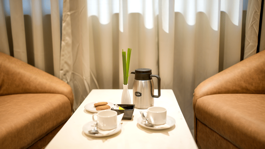 A close-up of a small table set for tea or coffee between two tan armchairs by a window at Pravasa Hotel, Kolhapur.