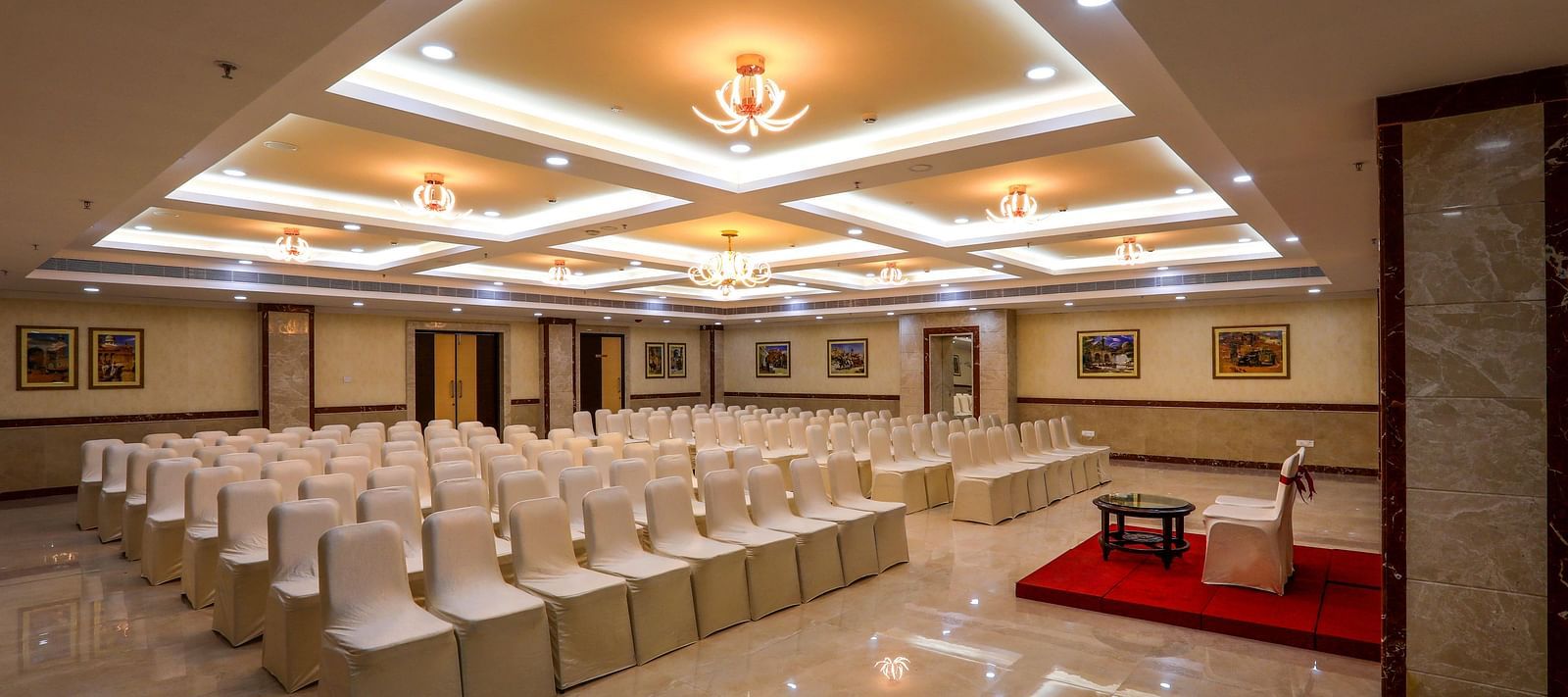 Front view of white chairs and a well-lit ceiling at Banquet Hall in Hotel Aadithya, Chennai