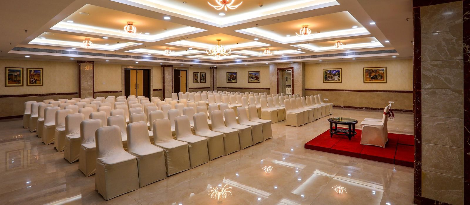 Front view of white chairs and a well-lit ceiling at Banquet Hall in Hotel Aadithya, Chennai