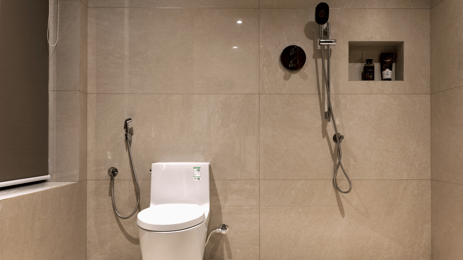 Bathroom at SUKAVI with a white toilet, hand bidet , light-colored tiled walls and floor, and a shower area with a wall-mounted shower system and toiletries.