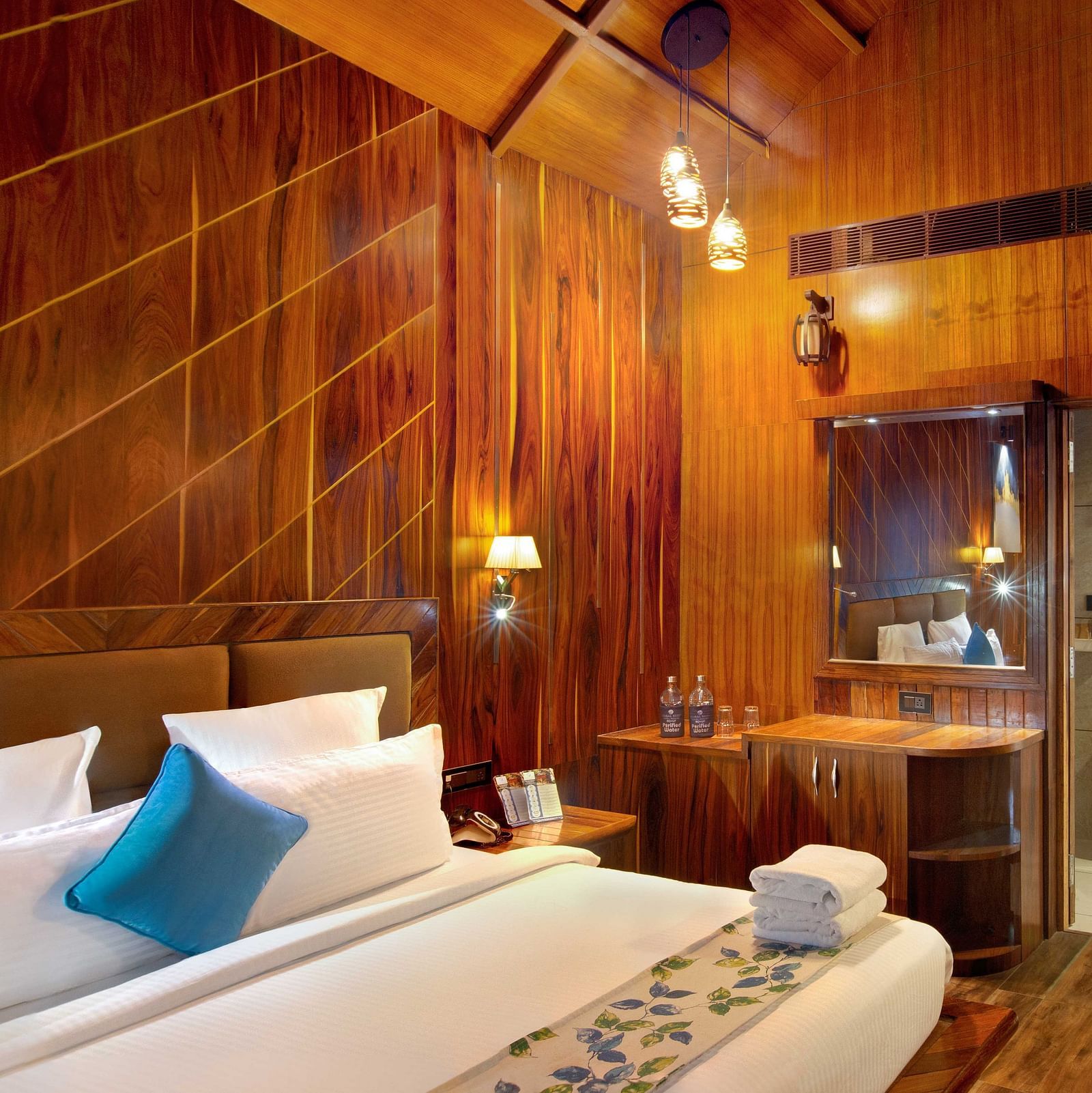 Angular shot of Coral Azure at Coral Reef Resort and Spa in Havelock featuring a double bed in the wooden-furnished room with a mirror next to it mounted on the wall beside which the door to the bathroom opens