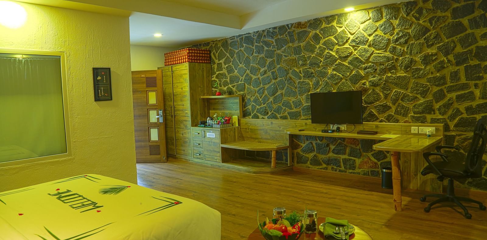 An image of a trail view room with a king size bed, chair, table, ceiling fan, flat screen TV, work desk, and bright lighting - Great Trails Yercaud by GRT Hotels