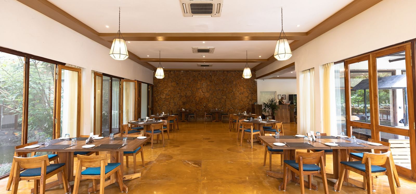 Seating arrangement in Azrak Restaurant at Saraca Resort & Spa Corbett with wooden flooring and wooden panelling on the ceiling alongside large French windows bringing in lots of light