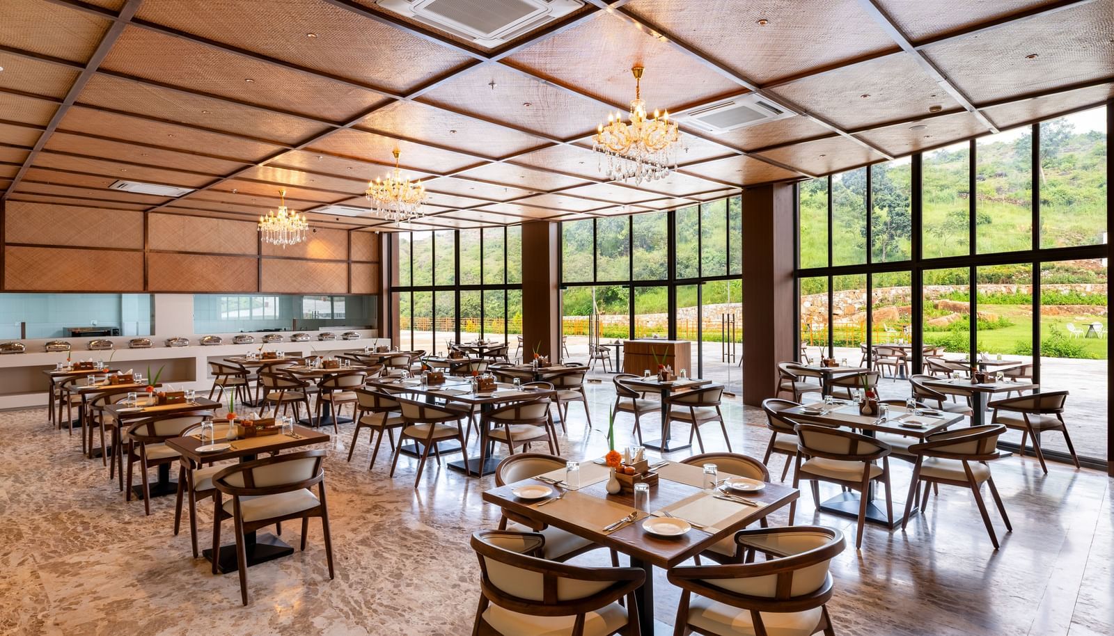 A side angle view of Lepra at Osian Valley Resort & Spa featuring a grid of wooden tables and chairs with white cushions. 
