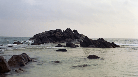 View of Mihiripenna Beach in Galle Sri Lanka with rocky outcrops, calm shallow waters, and a soft overcast sky in the background.