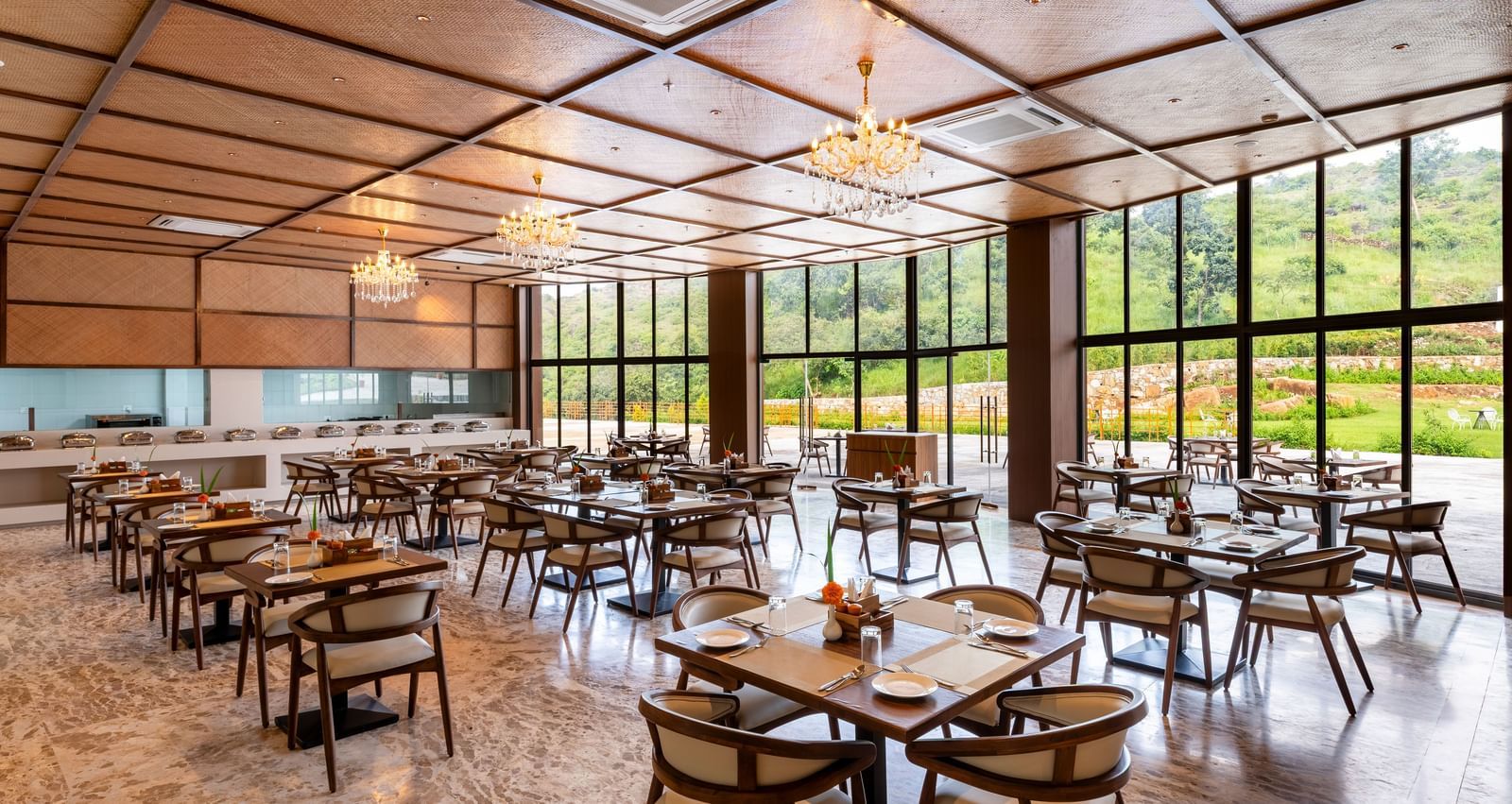 A side angle view of Lepra at Osian Valley Resort & Spa featuring a grid of wooden tables and chairs with white cushions. 