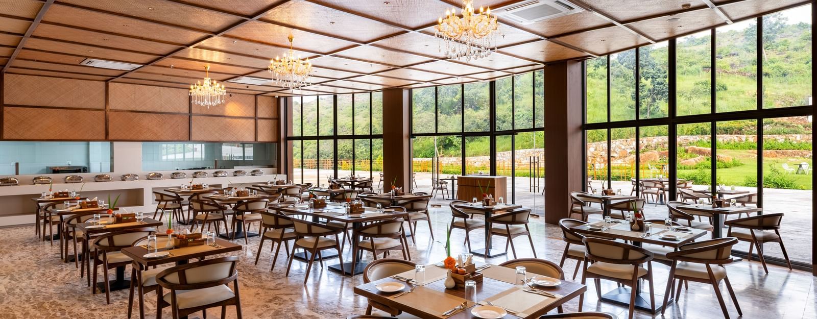 A side angle view of Lepra at Osian Valley Resort & Spa featuring a grid of wooden tables and chairs with white cushions. 