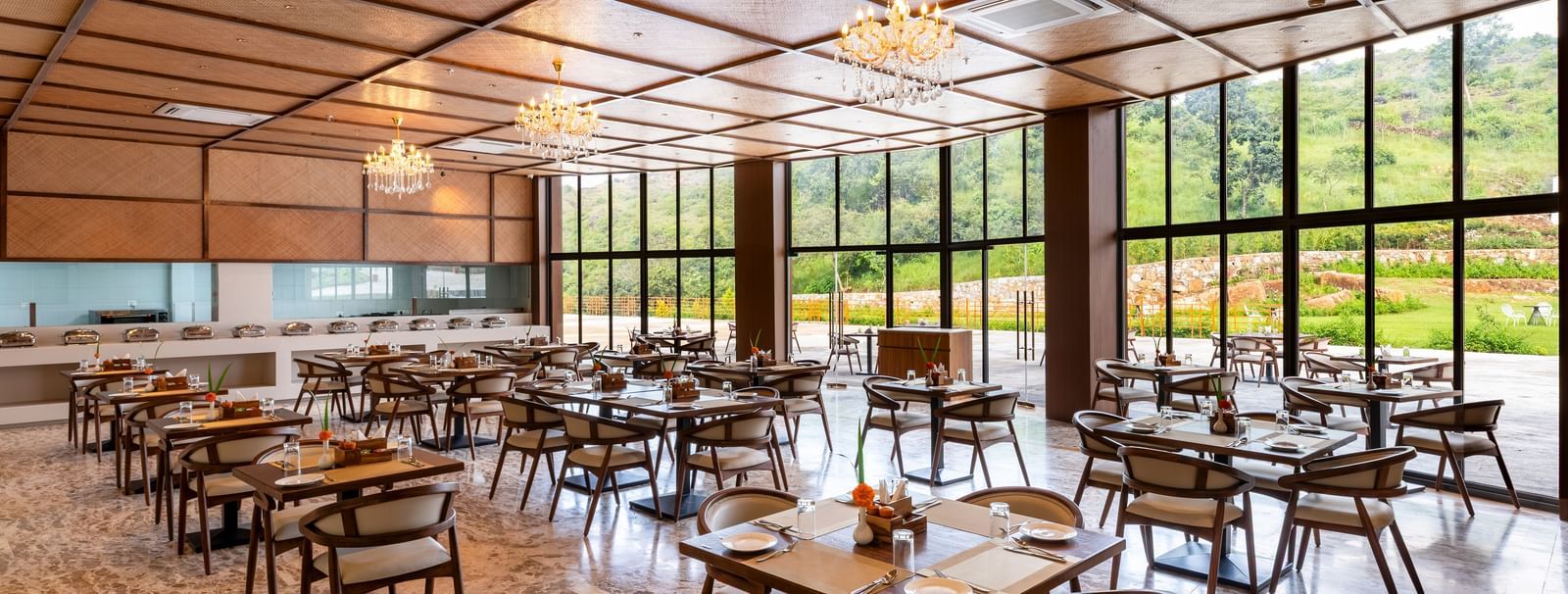 A side angle view of Lepra at Osian Valley Resort & Spa featuring a grid of wooden tables and chairs with white cushions. 