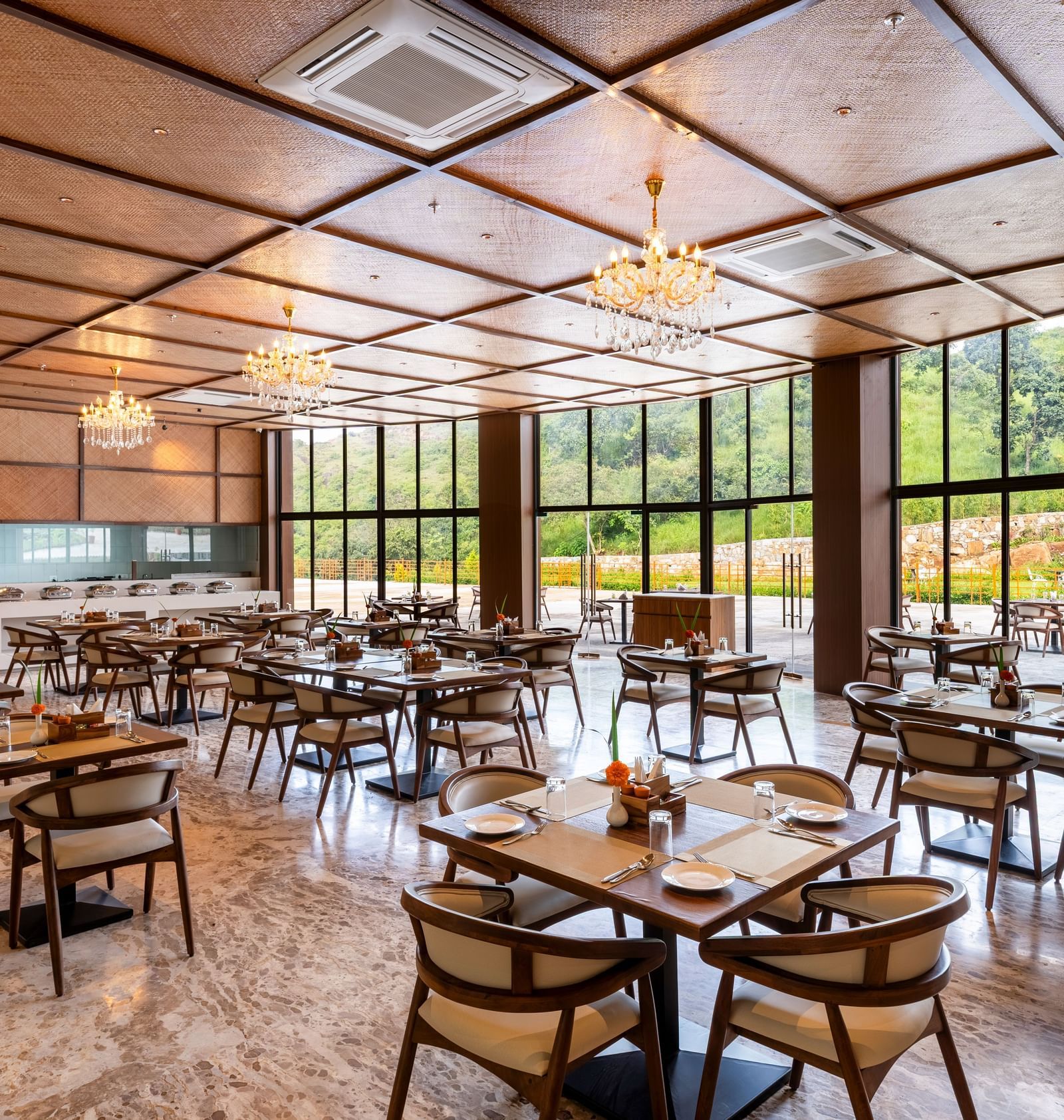 A side angle view of Lepra at Osian Valley Resort & Spa featuring a grid of wooden tables and chairs with white cushions. 