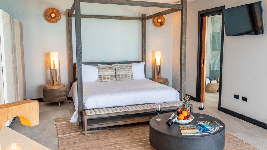 A bedroom at the Tamarind Hills Resort and Villas, Antigua, with a king size canopy bed, two nightstands, a table and a wall mounted television.