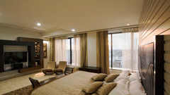 Bedroom of the Presidential Suite at The Piccadily Lucknow featuring a spacious bed, high-end entertainment console, floor-to-ceiling windows, and lounge chairs.