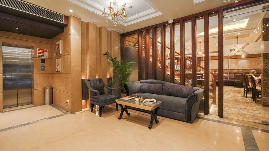 A hotel waiting area with dark sofas, a small coffee table, and a wooden slat screen separating the space from a lift area at BluSalzz Select City Centre, Amritsar.