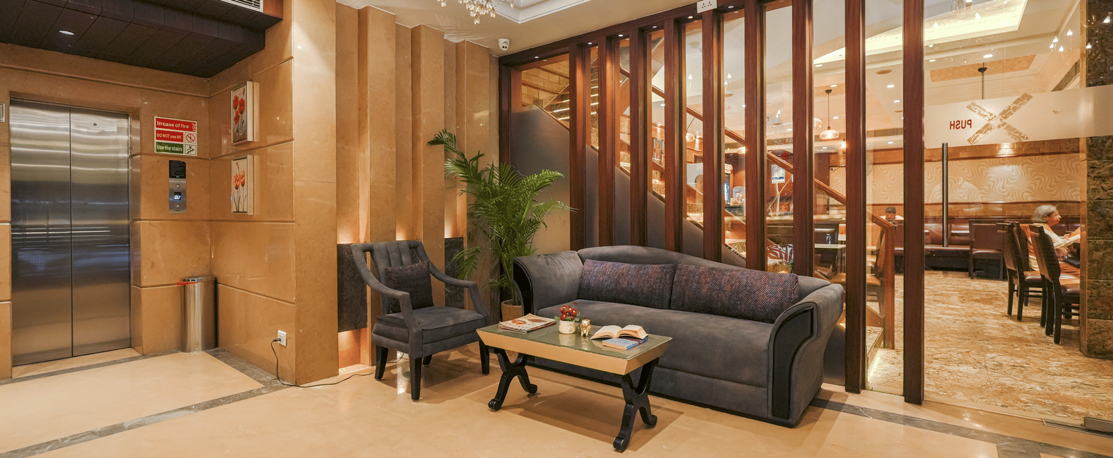 A hotel waiting area with dark sofas, a small coffee table, and a wooden slat screen separating the space from a lift area at BluSalzz Select City Centre, Amritsar.