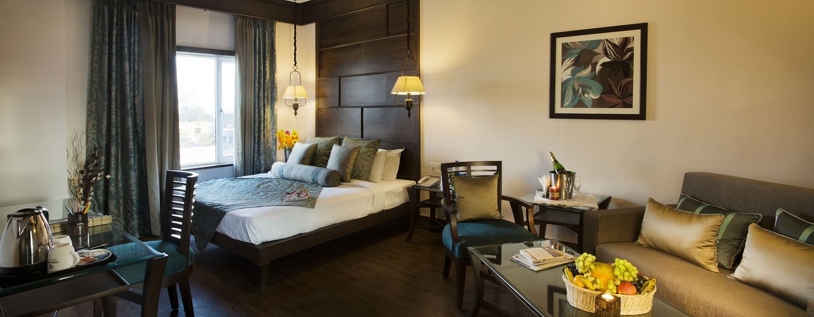 A bedroom with a a bed placed on the corner beside a large window and a sofa and a table - The Manor, Kashipur