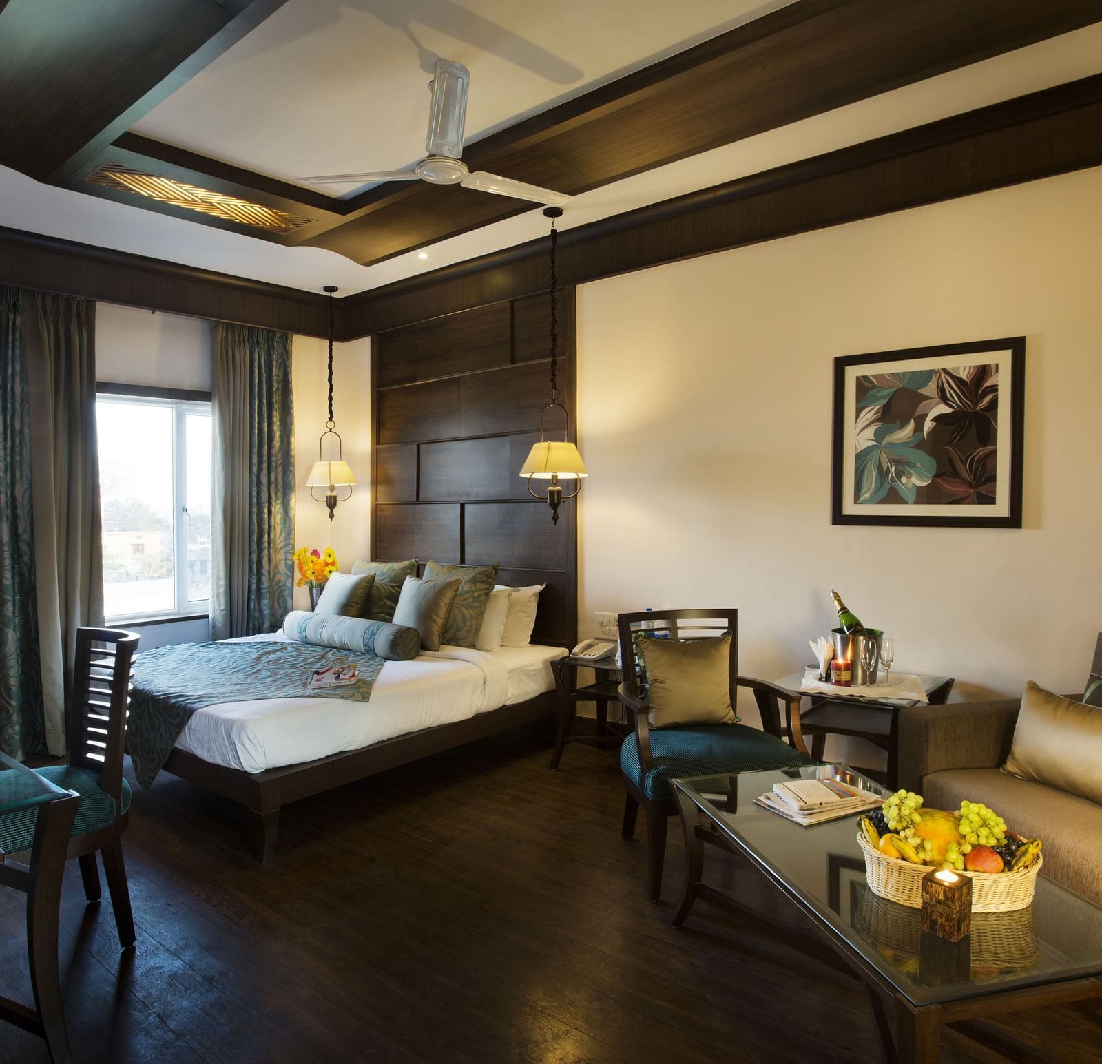 A bedroom with a a bed placed on the corner beside a large window and a sofa and a table - The Manor, Kashipur