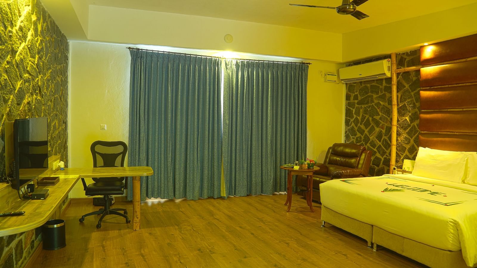 An image of a trail view room with a king size bed, chair, table, ceiling fan, flat screen TV, work desk, and bright lighting - Great Trails Yercaud by GRT Hotels - The Best Hotel in Yercaud