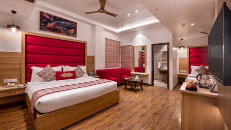 Front view of a Family Room at Lords Inn Amritsar with a king bed, red headboard panel, wooden flooring, ceiling fan, and warm ambient lighting.