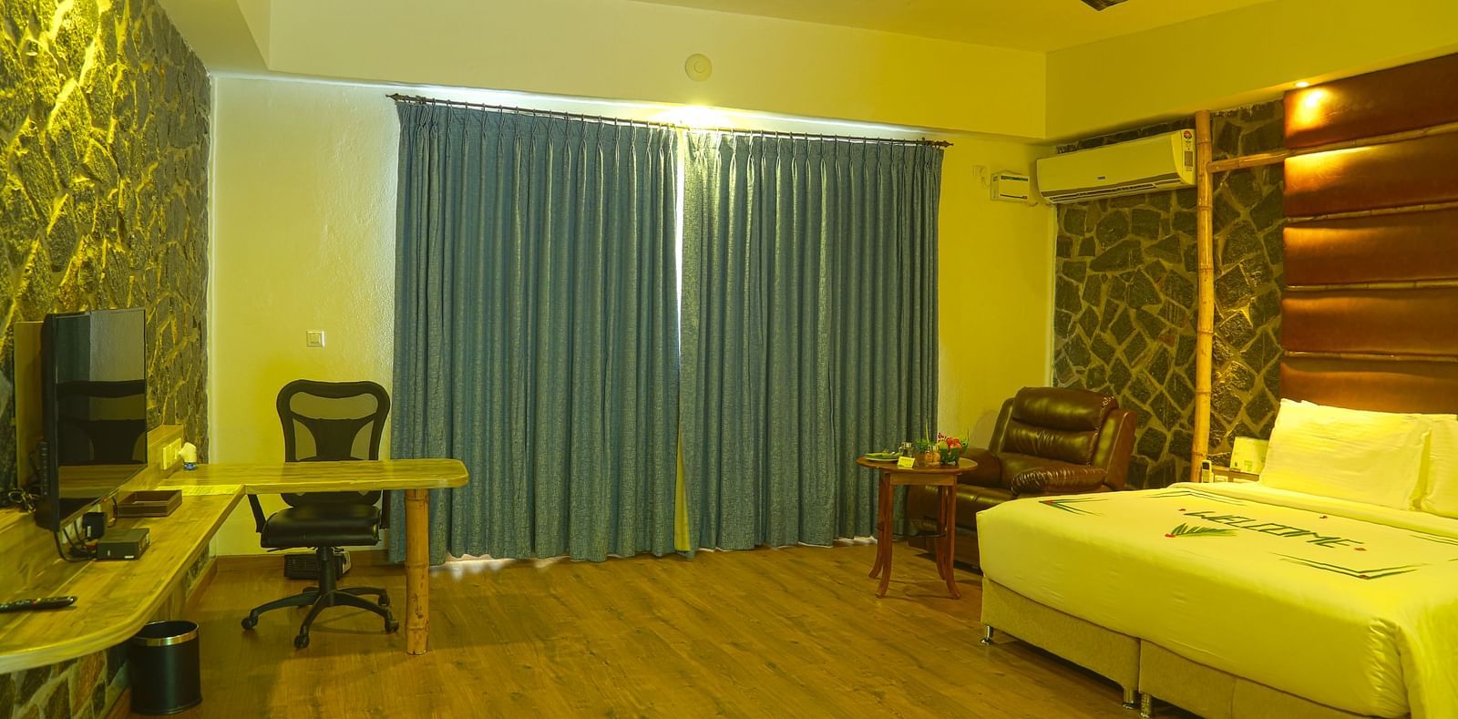 An image of a trail view room with a king size bed, chair, table, ceiling fan, flat screen TV, work desk, and bright lighting - Great Trails Yercaud by GRT Hotels - The Best Hotel in Yercaud