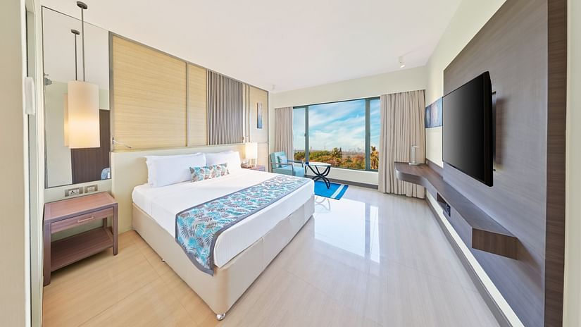 A full view of the bedroom with a bed, mirror on the wall and a huge glass window | The Resort