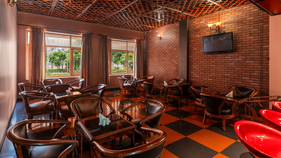 A seating lounge with wooden tables and chairs, brick walls, and a wall-mounted television at Amantra Shilpi Resort, Udaipur.
