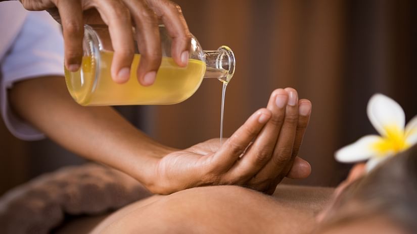 A person pours a liquid from a bottle onto their hand in a spa setting, with a flower nearby