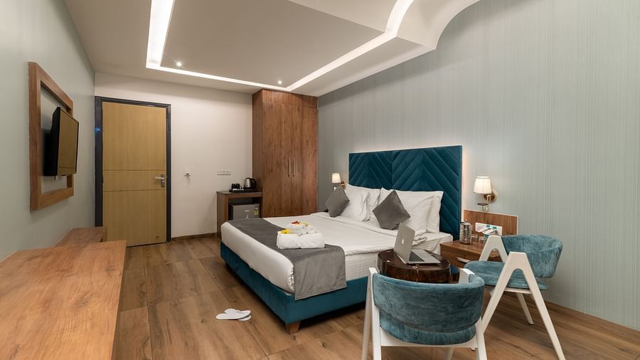 A shot of the premium room with a bed, bed side tables, wall mounted lamps, a flat screen TV, two chairs and a coffee table - DLS Ganga Bliss, Haridwar