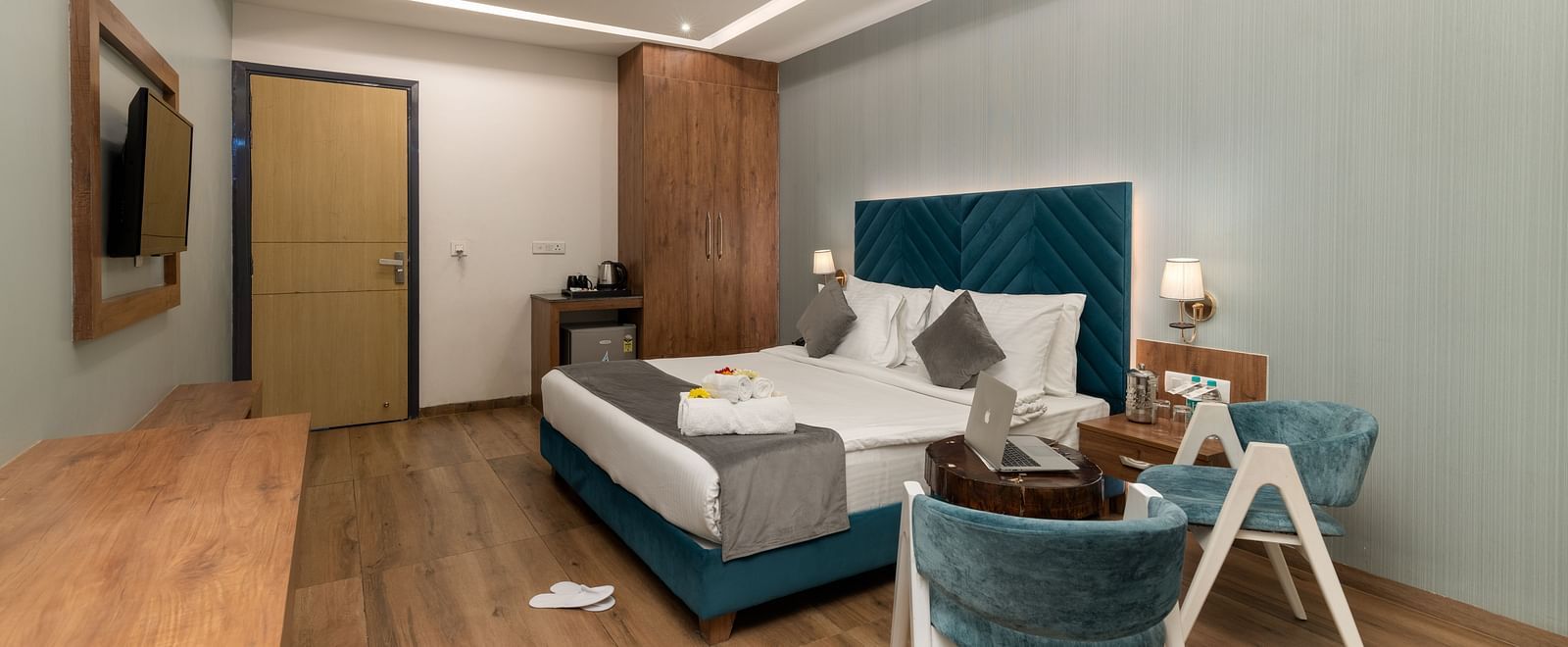 A shot of the premium room with a bed, bed side tables, wall mounted lamps, a flat screen TV, two chairs and a coffee table - DLS Ganga Bliss, Haridwar