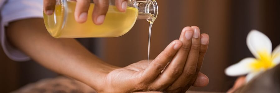 A person pours a liquid from a bottle onto their hand in a spa setting, with a flower nearby