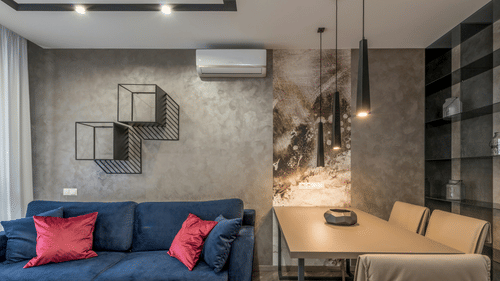 Modern suite living area with blue sofa, dining table, pendant lights, wall art, and contemporary decor.