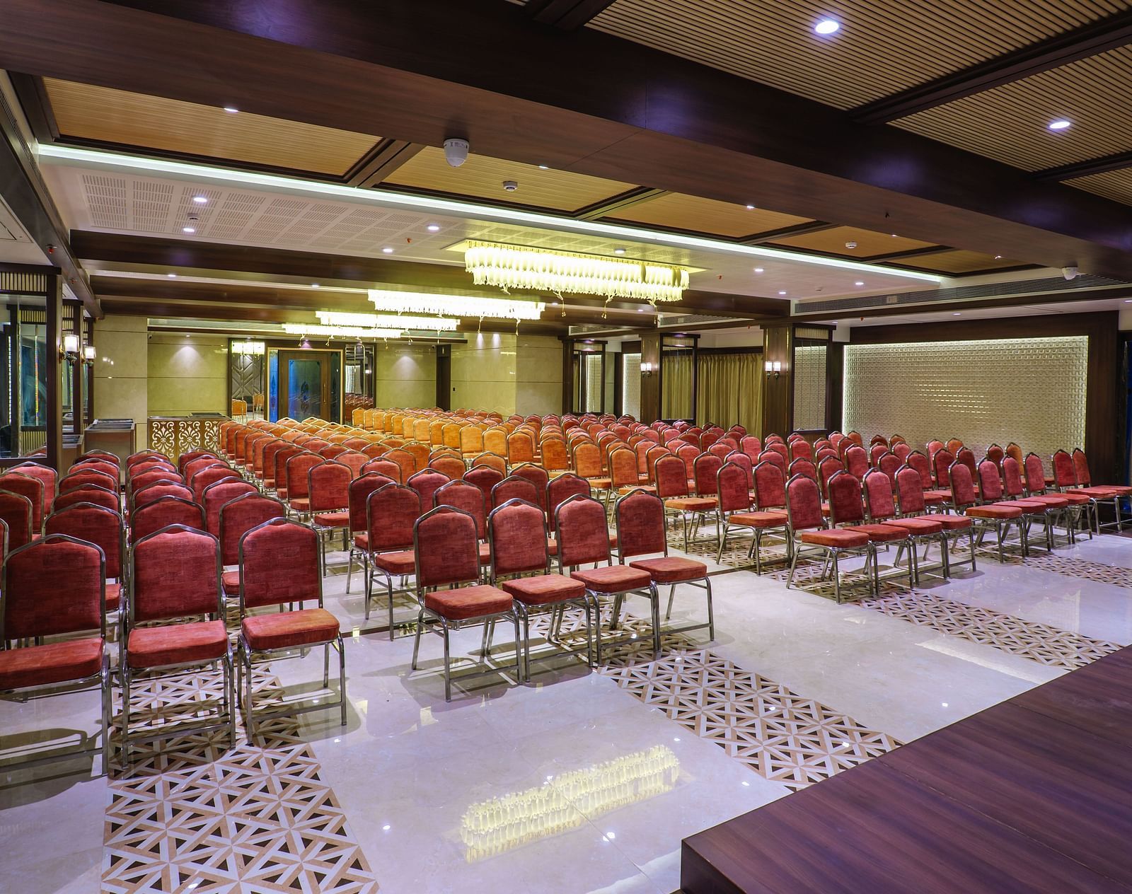 A large room is set up with rows of red chairs facing a stage area with warm lighting - Melior Inn