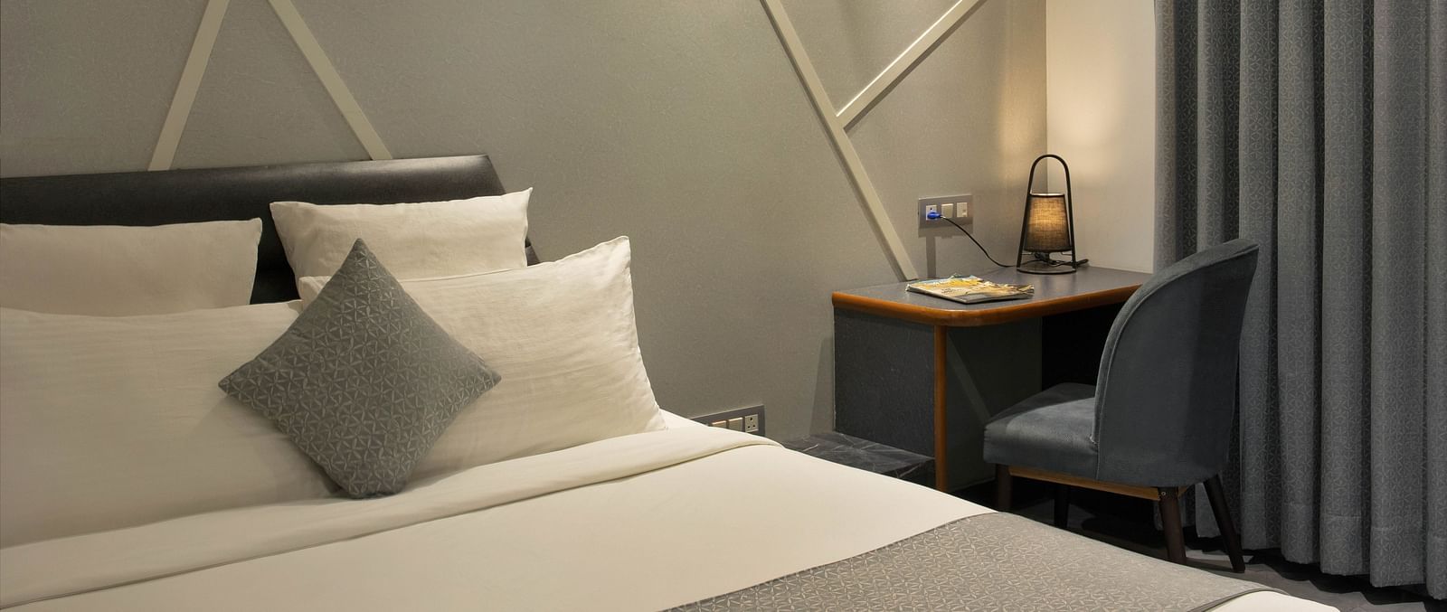 angular shot of Coral Deluxe Room at Coral Reef Hotel and Spa in Port Blair featuring a plush bed next to which a work desk and chair is placed near the window