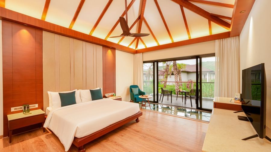 A spacious modern bedroom with a king-size bed, wooden flooring, and a balcony with glass doors at Ananta Spa and Resort, Ajabgarh.