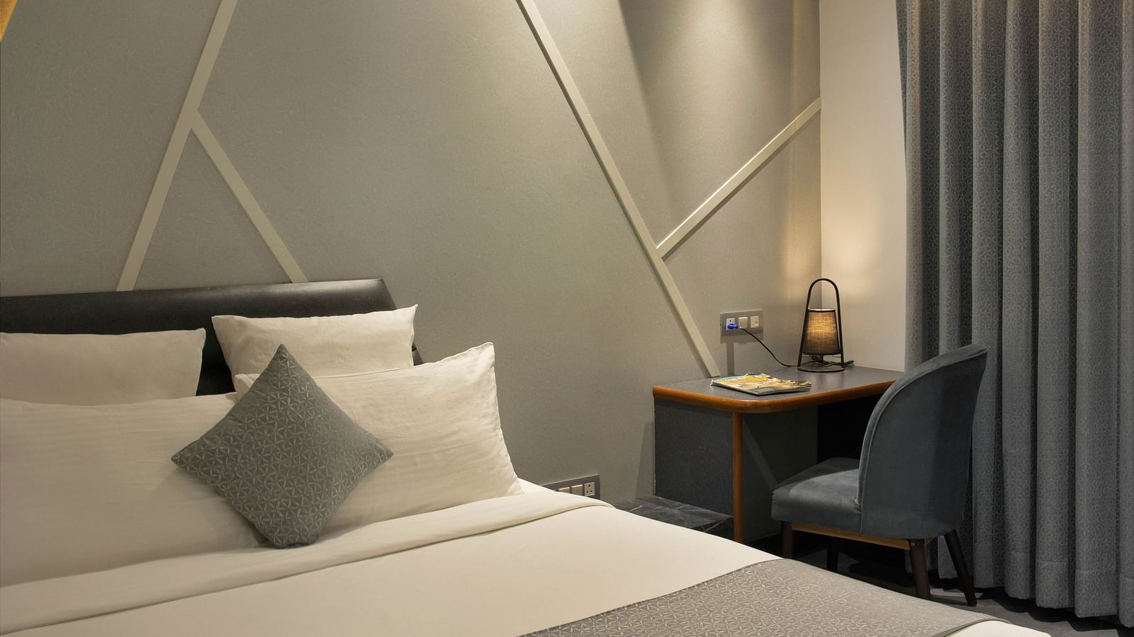 angular shot of Coral Deluxe Room at Coral Reef Hotel and Spa in Port Blair featuring a plush bed next to which a work desk and chair is placed near the window