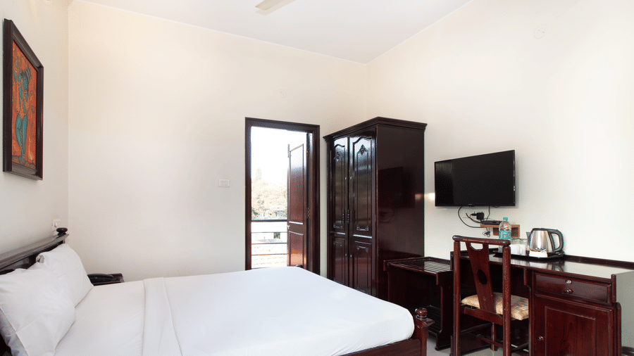 Hotel room with a double bed, a wall-mounted television, and a wooden dresser at Sanctum Suites Indiranagar, Bangalore.
