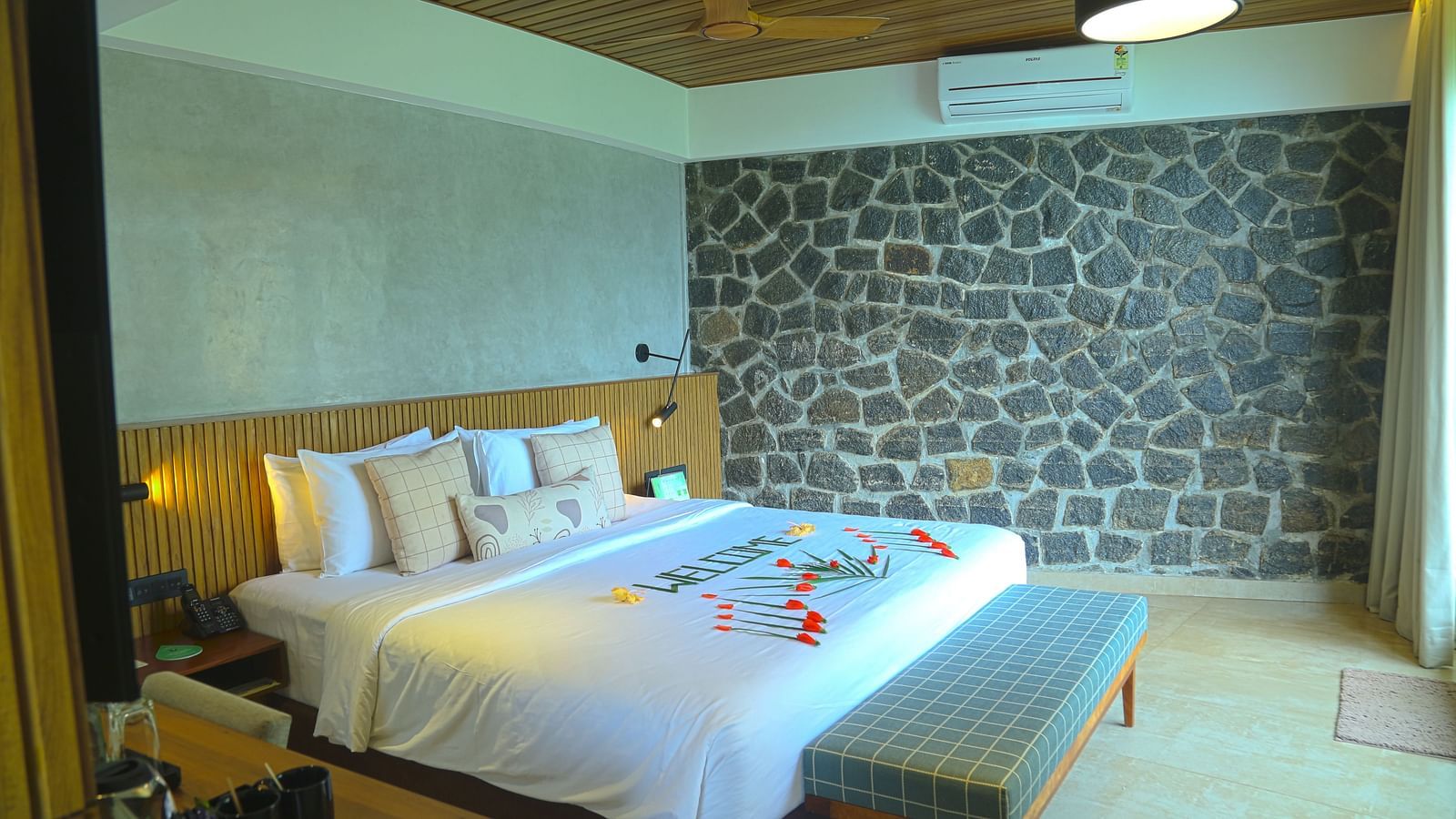 An image of the pent house with a king size bed, bed side table, couch, a light hanging from the ceiling, and a wall with stone finish - Great Trails Yercaud by GRT Hotels