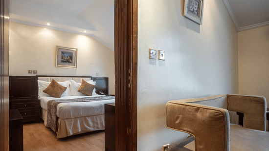Suite at Boma Inn Nairobi featuring a doorway into the bedroom with a plush bed under warm lighting from another room with a wall hanging over a sofa