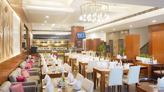 Elegant restaurant interior at Nemesia featuring chandeliers, wooden furniture, tables arranged with napkins, water glasses, and plates.