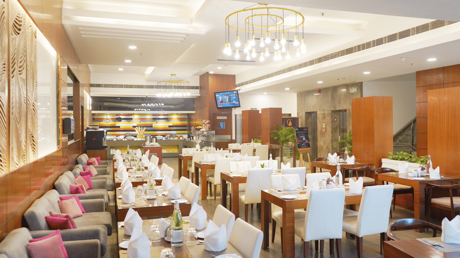Elegant restaurant interior at Nemesia featuring chandeliers, wooden furniture, tables arranged with napkins, water glasses, and plates.