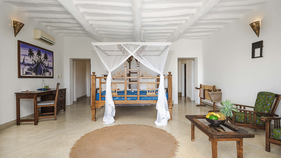 A bright hotel room with a wooden four-poster bed, a desk, and a seating area with wooden armchairs and a coffee table - Shooting Star Boutique Hotel.