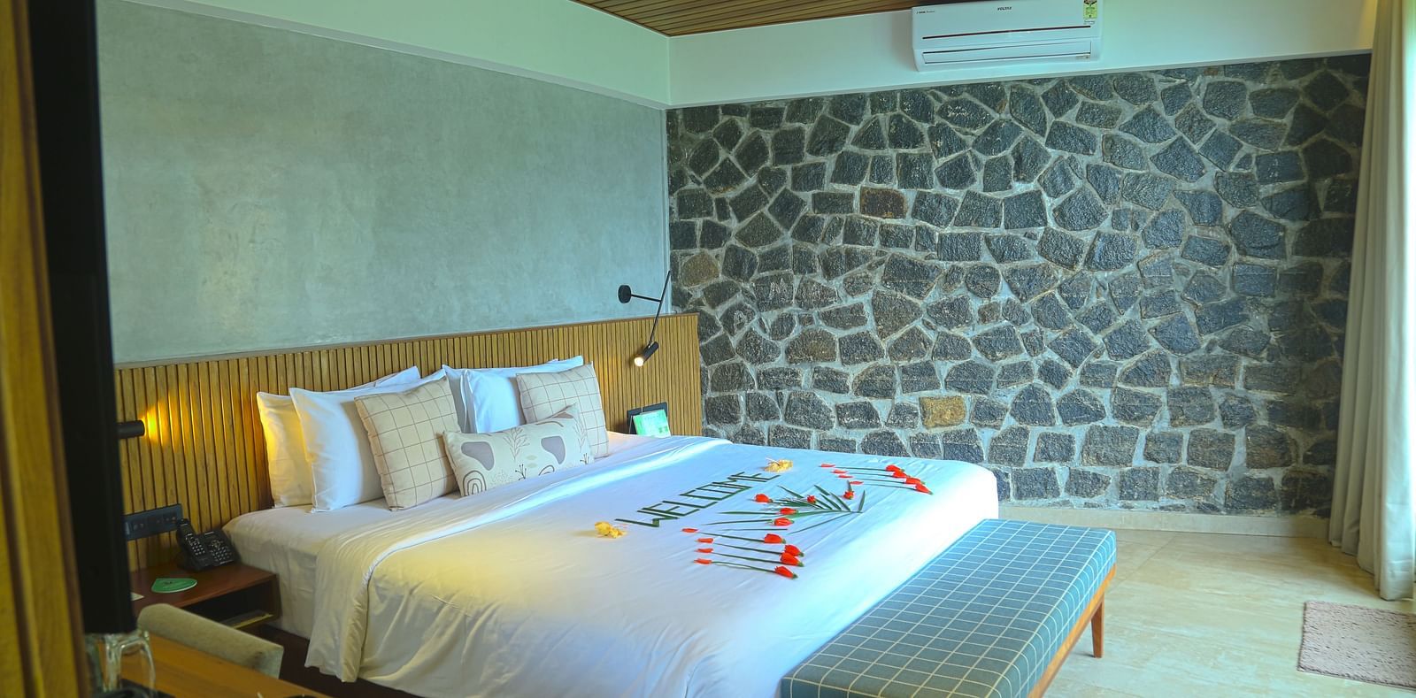 An image of the pent house with a king size bed, bed side table, couch, a light hanging from the ceiling, and a wall with stone finish - Great Trails Yercaud by GRT Hotels