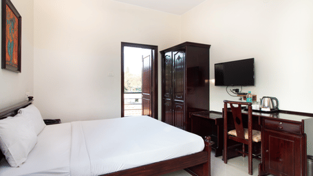 Hotel room with a double bed, a wall-mounted television, and a wooden dresser at Sanctum Suites Indiranagar, Bangalore.