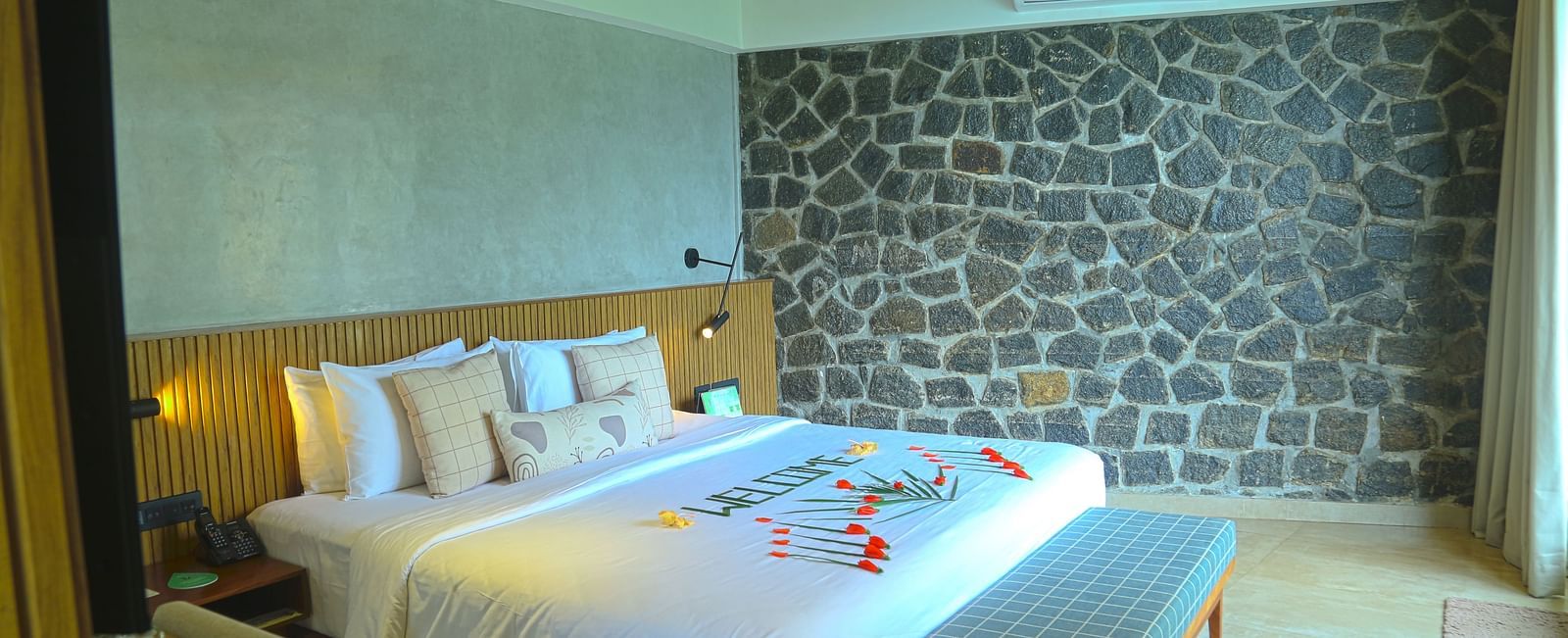 An image of the pent house with a king size bed, bed side table, couch, a light hanging from the ceiling, and a wall with stone finish - Great Trails Yercaud by GRT Hotels