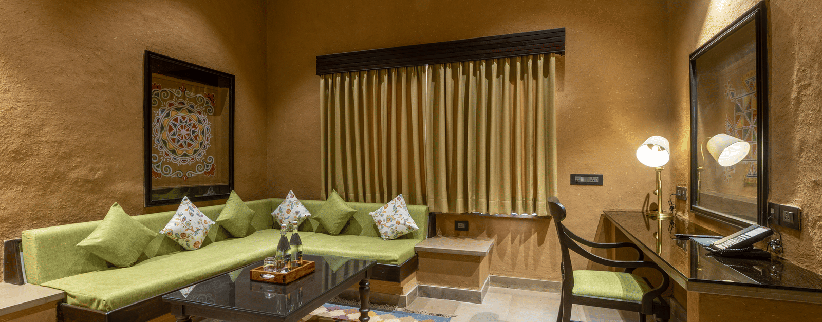 A cosy living area at Aamaghati Wildlife Resort with green sofas, patterned rugs, and tasteful décor designed for relaxation.