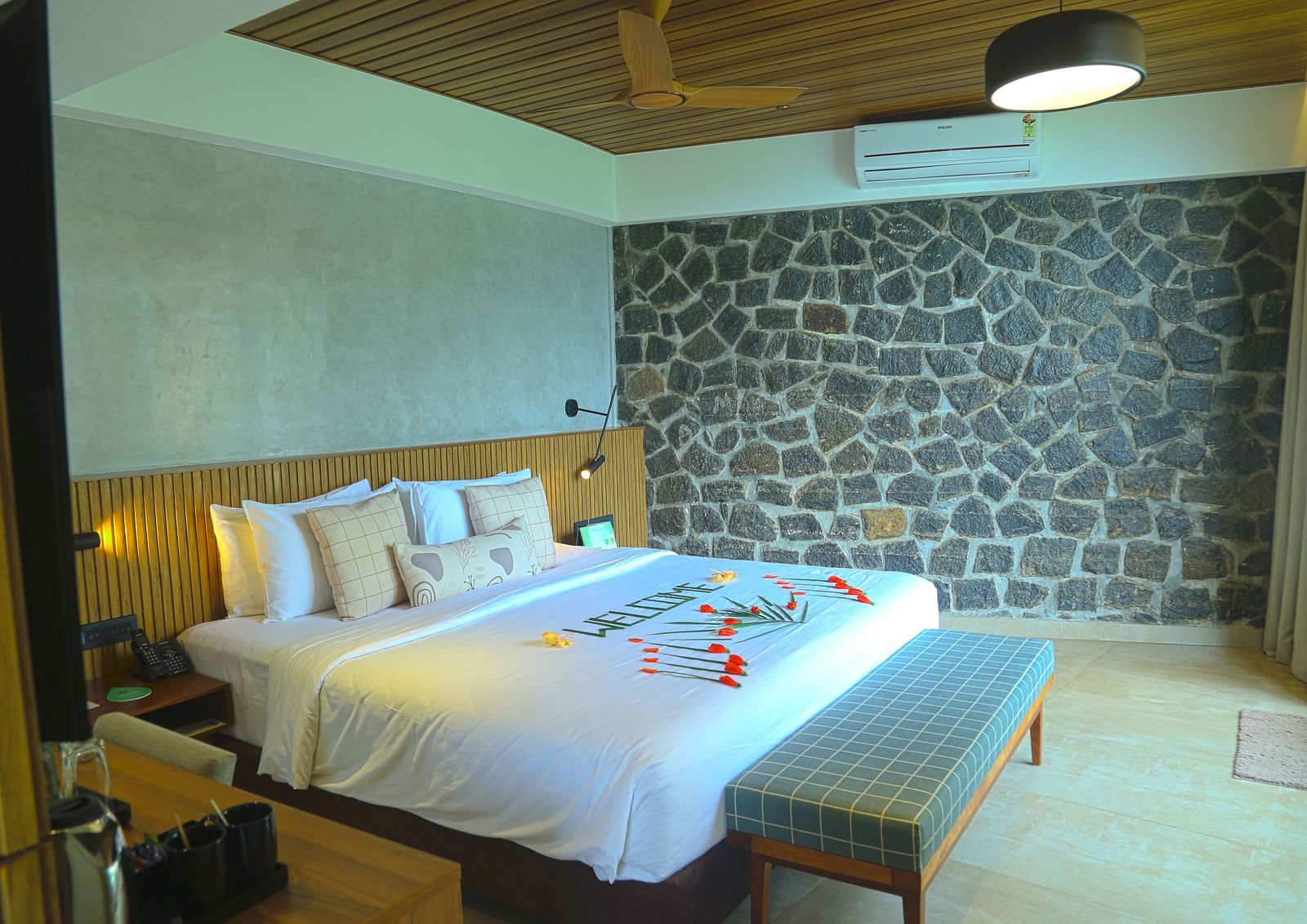 An image of the pent house with a king size bed, bed side table, couch, a light hanging from the ceiling, and a wall with stone finish - Great Trails Yercaud by GRT Hotels