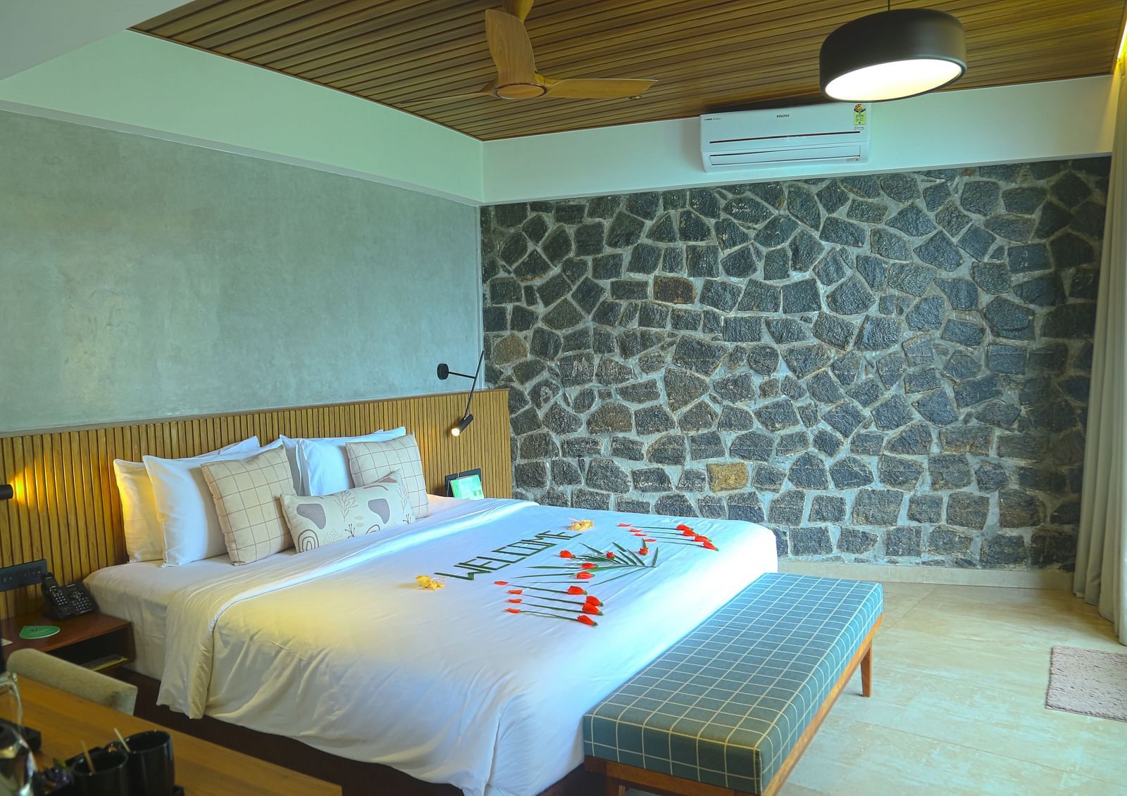 An image of the pent house with a king size bed, bed side table, couch, a light hanging from the ceiling, and a wall with stone finish - Great Trails Yercaud by GRT Hotels