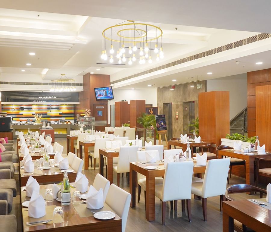 Elegant restaurant interior at Nemesia featuring chandeliers, wooden furniture, tables arranged with napkins, water glasses, and plates.
