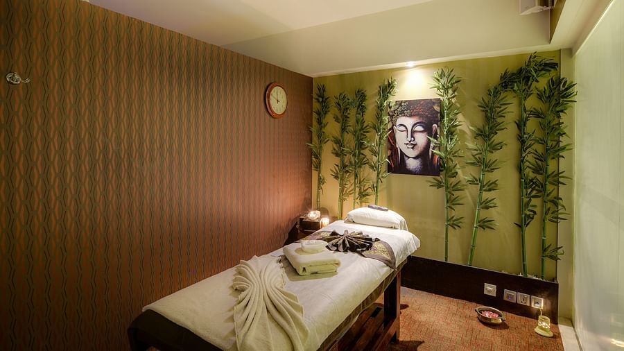 Image of a massage bed with towels on it and a photo of Lord Buddha on the wall behind it with artificial creepers hanging on the wall at Pride Hotel Bangalore
