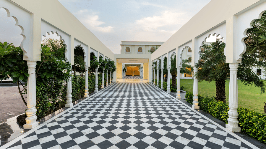 A chequered pathway leading to the entrance of Beelwa Palace, Jaipur, surrounded by lush green lawns on either sides of it.