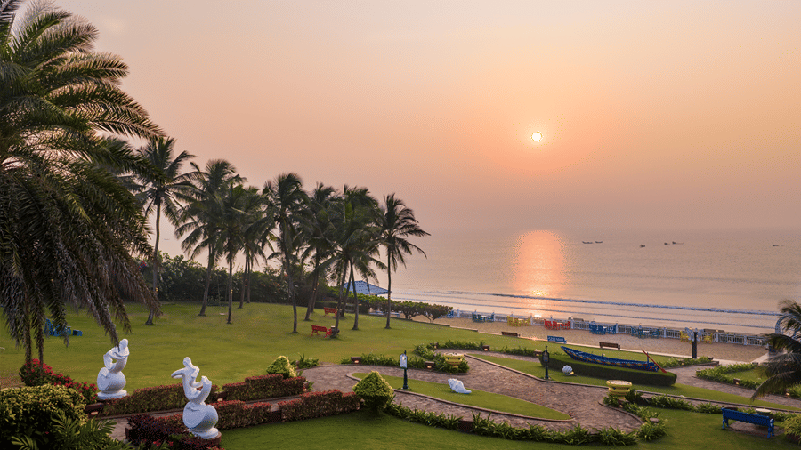 Scenic view of the sun setting over the ocean beside manicured lawns and palm trees at MAYFAIR Palm Beach Resort, Gopalpur-on-Sea. 